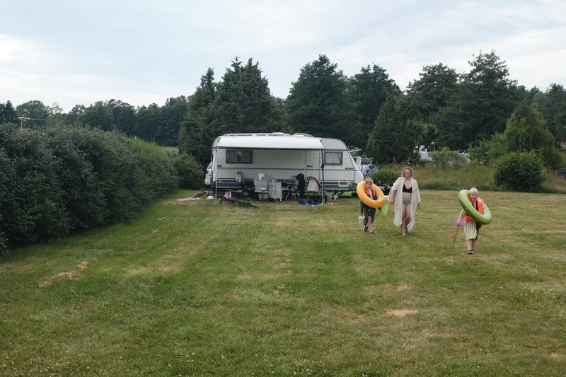 Family walking on a grassy field near a parked camper van with trees in the background.